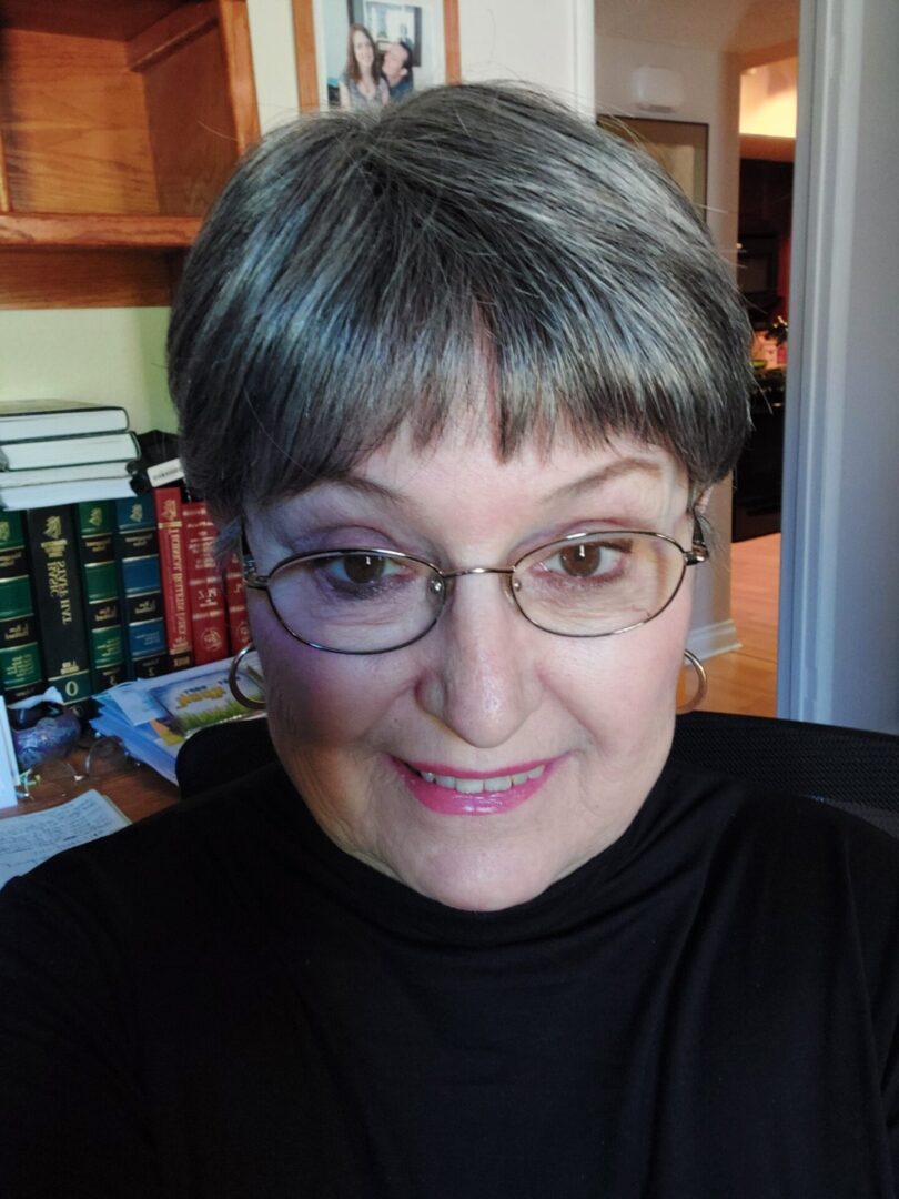 A woman with glasses and short hair sitting in front of books.